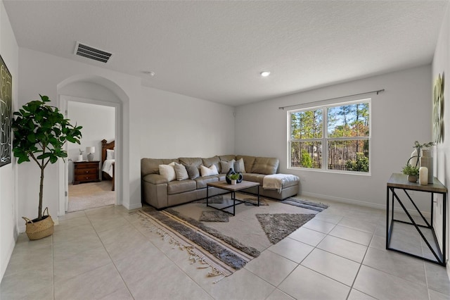 living area with light tile patterned floors, visible vents, arched walkways, and a textured ceiling