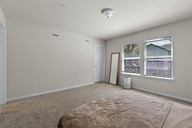 unfurnished bedroom featuring light carpet, a textured ceiling, and baseboards