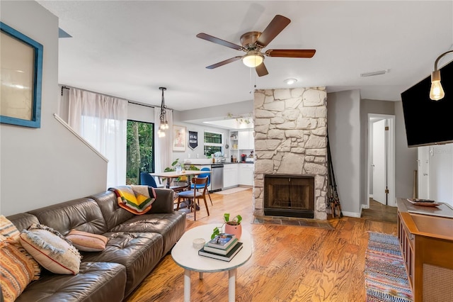 living area with visible vents, a ceiling fan, a fireplace, and light wood finished floors