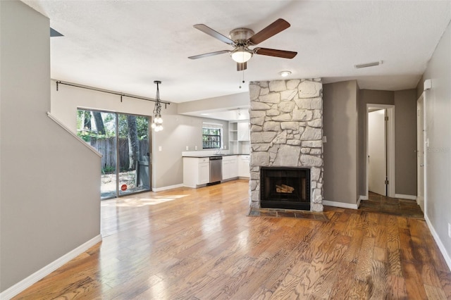 unfurnished living room with visible vents, baseboards, ceiling fan, a stone fireplace, and light wood-style floors