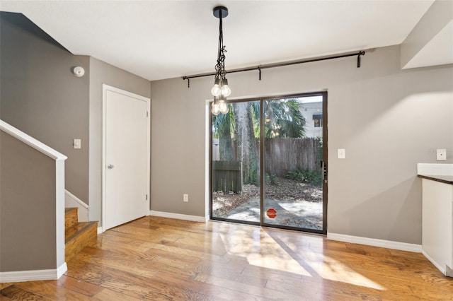 unfurnished dining area with stairway, baseboards, an inviting chandelier, and wood finished floors