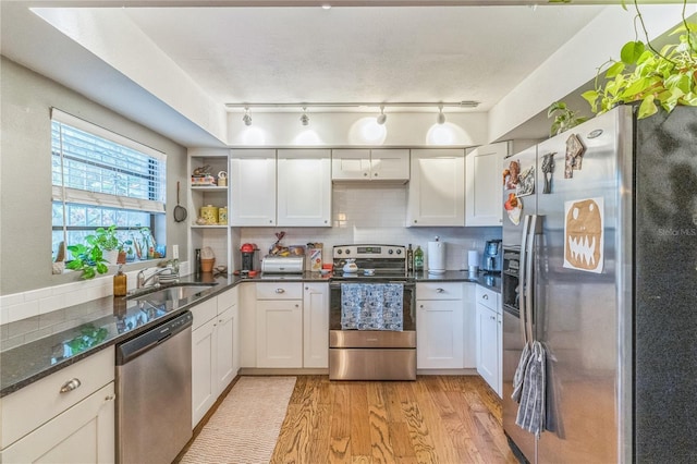 kitchen with light wood finished floors, a sink, decorative backsplash, stainless steel appliances, and open shelves