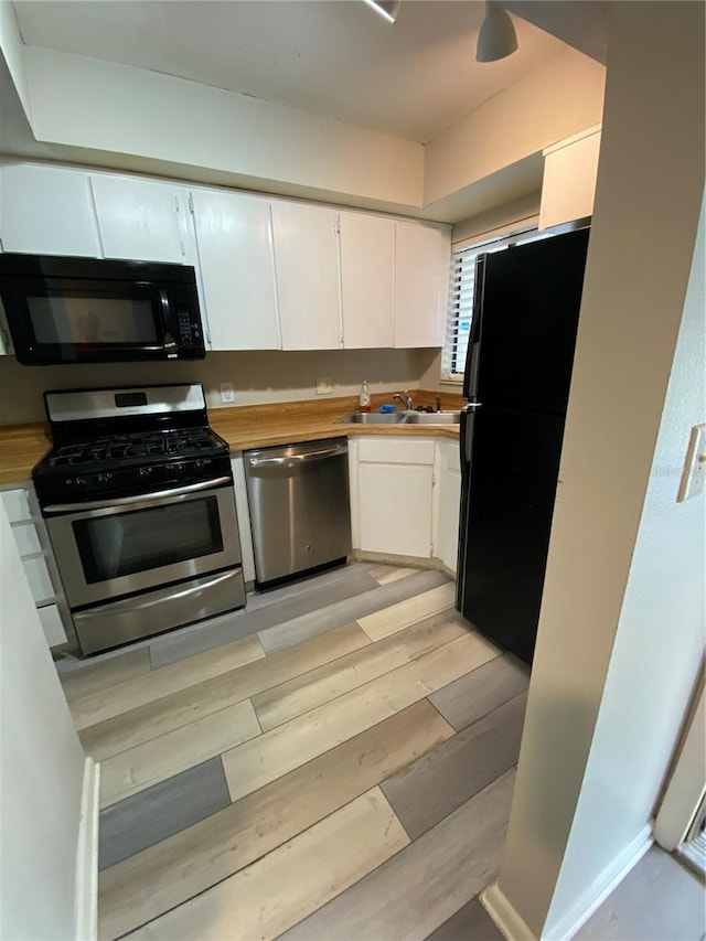 kitchen with a sink, black appliances, white cabinets, light wood-style floors, and wood counters