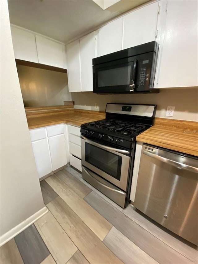 kitchen with light wood-type flooring, appliances with stainless steel finishes, butcher block counters, and white cabinetry