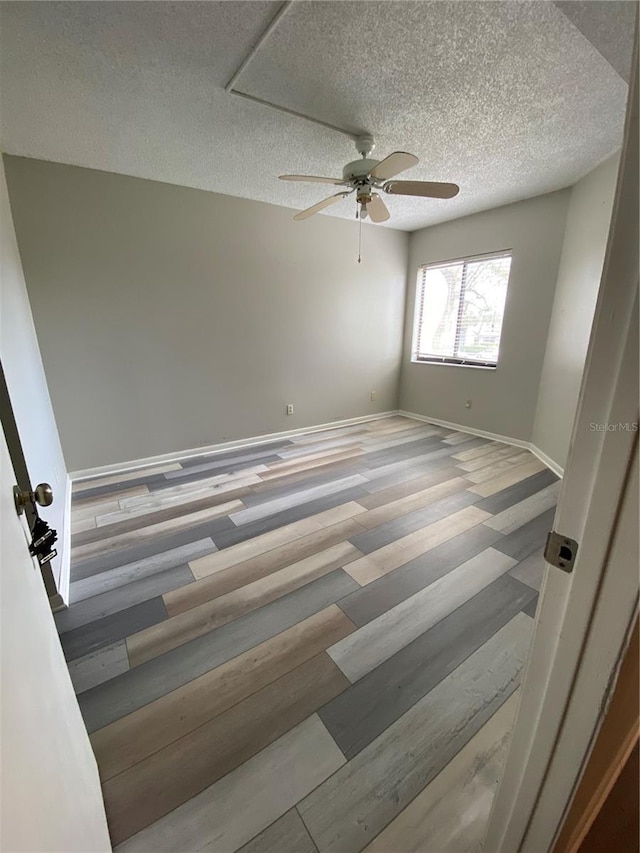 spare room with baseboards, a textured ceiling, wood finished floors, and a ceiling fan