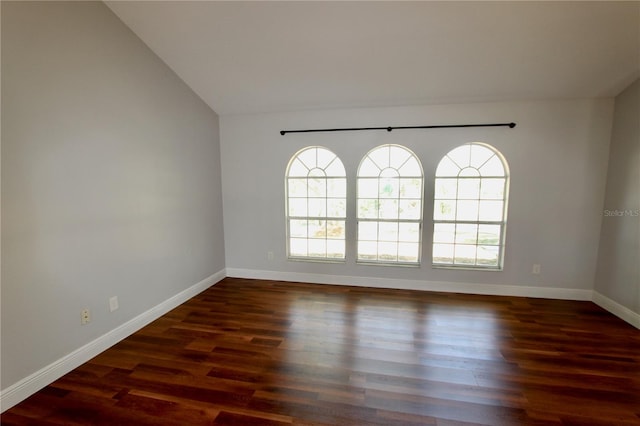 spare room featuring dark wood finished floors, lofted ceiling, and baseboards