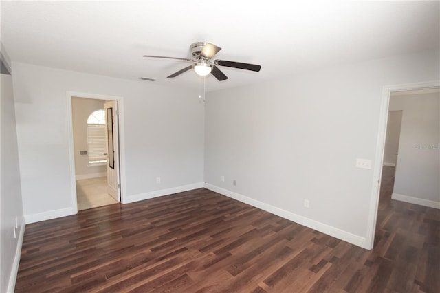 unfurnished room with a ceiling fan, visible vents, dark wood-style flooring, and baseboards