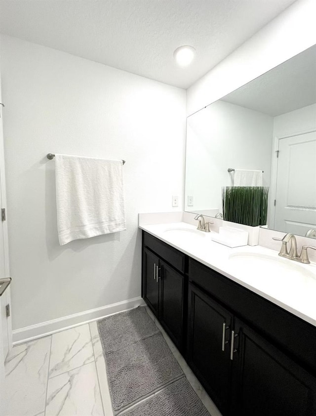 full bath featuring double vanity, marble finish floor, baseboards, and a sink