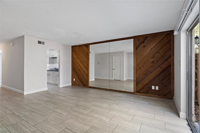 empty room featuring baseboards, visible vents, wood walls, and a sink