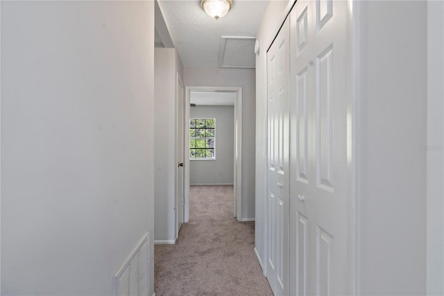 corridor with visible vents, light colored carpet, a textured ceiling, and baseboards