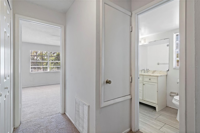 hallway featuring visible vents, light colored carpet, and baseboards