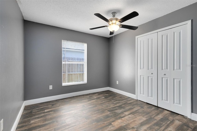 unfurnished bedroom featuring a textured ceiling, dark wood-style floors, a closet, and baseboards