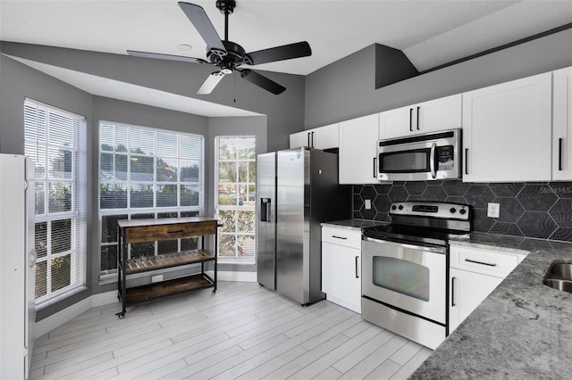 kitchen with backsplash, vaulted ceiling, stone counters, white cabinets, and stainless steel appliances