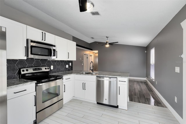 kitchen featuring tasteful backsplash, lofted ceiling, a peninsula, stainless steel appliances, and a sink