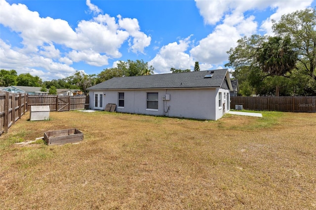 rear view of property featuring a fenced backyard, a lawn, a vegetable garden, and stucco siding