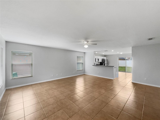 unfurnished living room with tile patterned flooring, a ceiling fan, visible vents, and a wealth of natural light