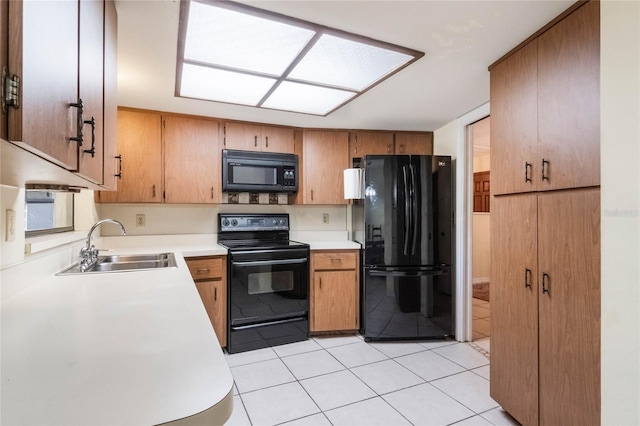 kitchen with brown cabinets, black appliances, a sink, light countertops, and light tile patterned floors