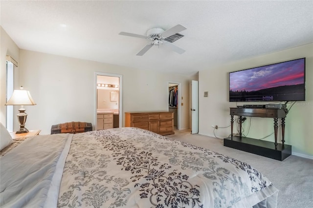 bedroom featuring light carpet, a ceiling fan, ensuite bath, baseboards, and a spacious closet