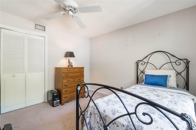 bedroom with visible vents, light colored carpet, a closet, a textured ceiling, and a ceiling fan