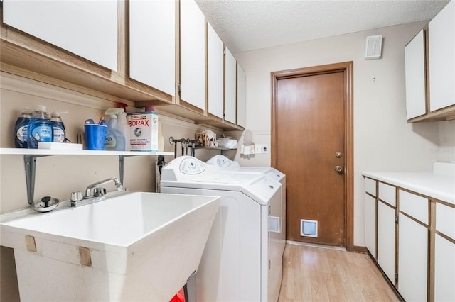 laundry area featuring washer and clothes dryer, light wood-style floors, cabinet space, a textured ceiling, and a sink