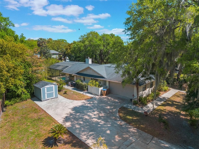 view of front of property featuring an outbuilding, a chimney, concrete driveway, a garage, and a storage shed