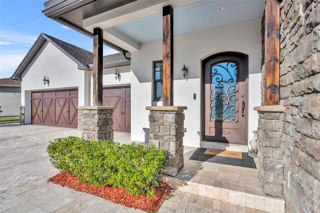 doorway to property with a garage, decorative driveway, and stucco siding