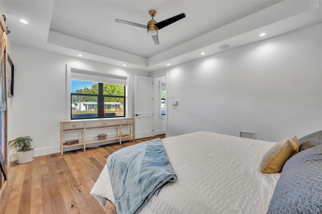 bedroom featuring visible vents, a tray ceiling, wood finished floors, recessed lighting, and baseboards