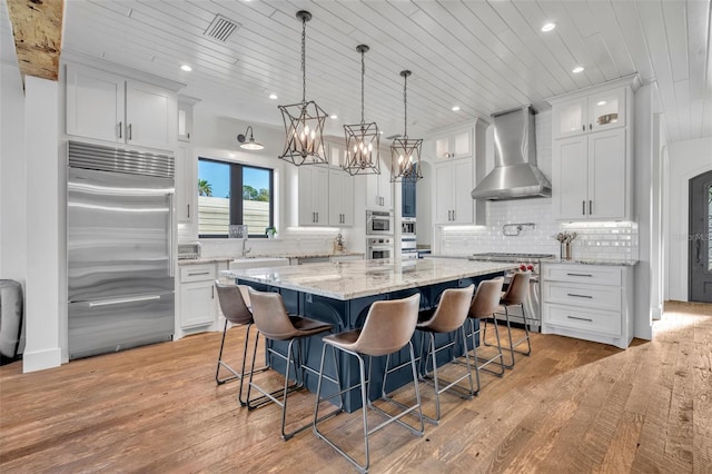 kitchen featuring visible vents, high end appliances, white cabinets, and wall chimney range hood