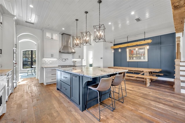 kitchen with wood ceiling, white cabinetry, wall chimney exhaust hood, backsplash, and a center island