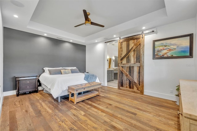 bedroom featuring light wood-type flooring, a barn door, a raised ceiling, and baseboards