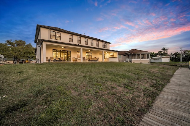 back of house at dusk with an outdoor living space, ceiling fan, stucco siding, a lawn, and a patio area