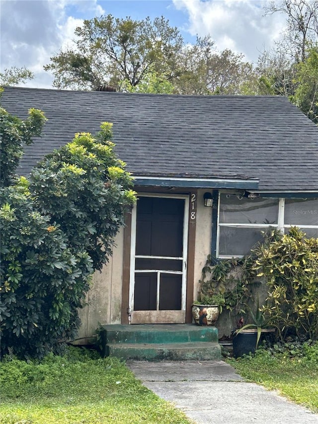 view of exterior entry featuring roof with shingles and stucco siding