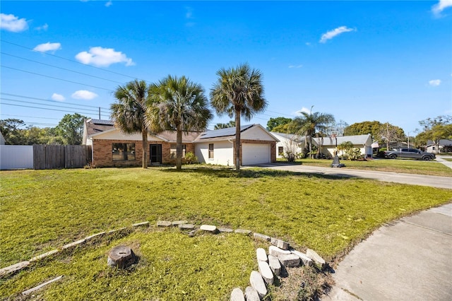 ranch-style home featuring a front lawn, driveway, roof mounted solar panels, fence, and brick siding