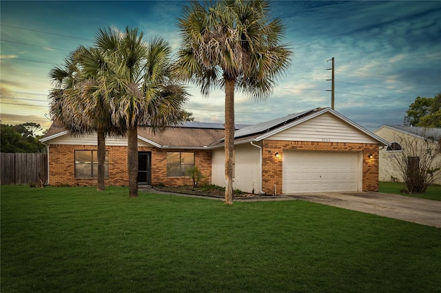ranch-style home with concrete driveway, a yard, brick siding, and roof mounted solar panels