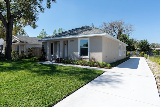 single story home featuring stucco siding, driveway, fence, a front yard, and a shingled roof