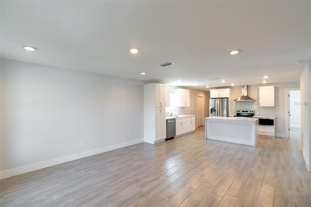 kitchen with visible vents, wall chimney range hood, open floor plan, appliances with stainless steel finishes, and a sink