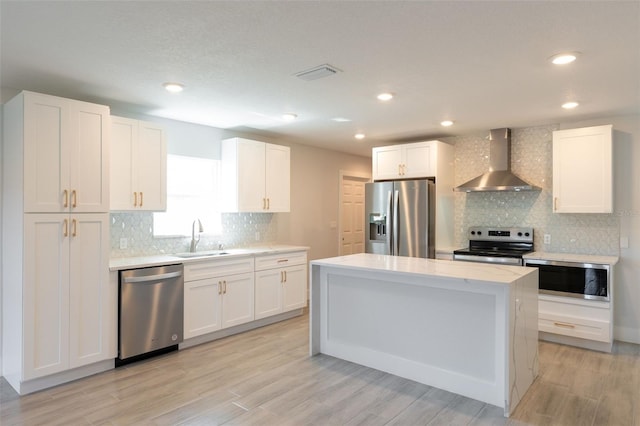 kitchen with visible vents, a kitchen island, white cabinets, appliances with stainless steel finishes, and wall chimney exhaust hood