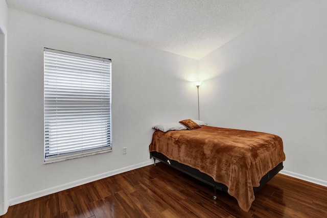 bedroom with a textured ceiling, wood finished floors, and baseboards
