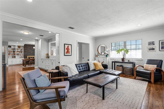 living room featuring visible vents, built in shelves, ornamental molding, a textured ceiling, and hardwood / wood-style floors