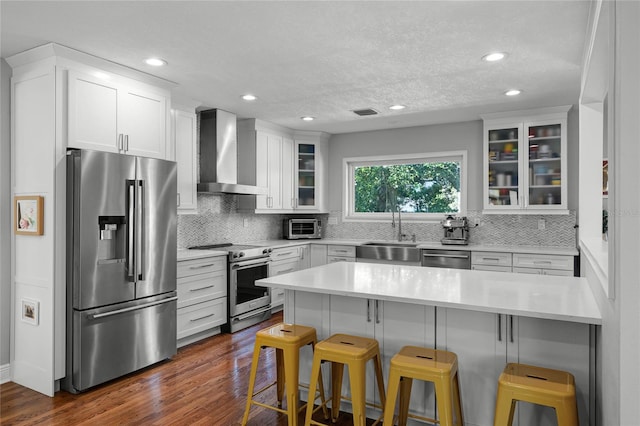 kitchen featuring wall chimney range hood, a breakfast bar area, appliances with stainless steel finishes, white cabinetry, and a sink