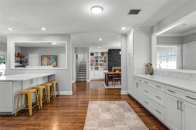 kitchen featuring dark wood-style floors, visible vents, white cabinetry, light countertops, and a kitchen bar