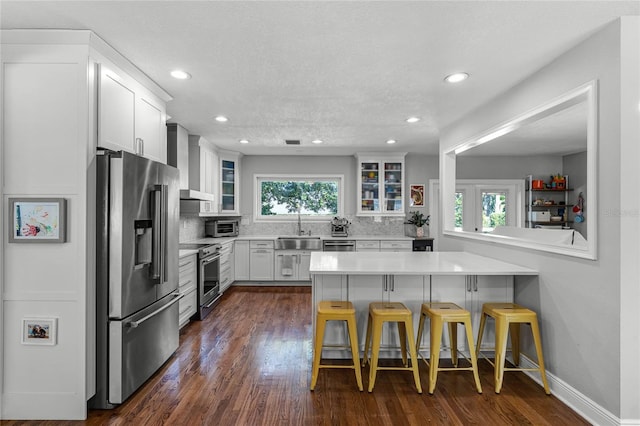 kitchen featuring glass insert cabinets, a breakfast bar, a wealth of natural light, stainless steel appliances, and wall chimney exhaust hood