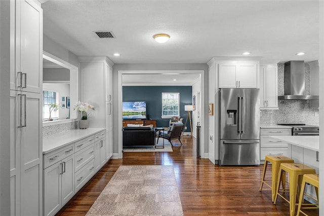 kitchen featuring dark wood finished floors, stainless steel appliances, light countertops, wall chimney range hood, and backsplash