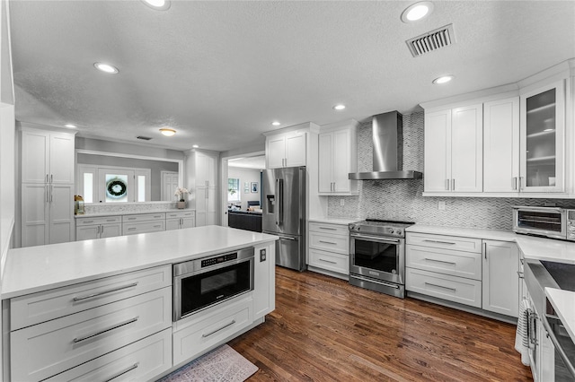 kitchen with stainless steel appliances, visible vents, light countertops, and wall chimney range hood