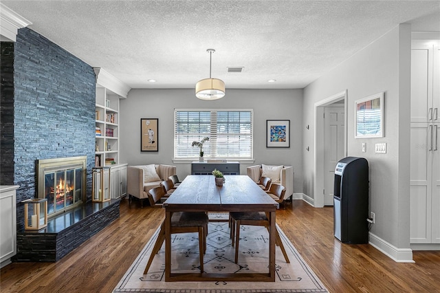 dining space featuring dark wood finished floors, a stone fireplace, baseboards, and a textured ceiling