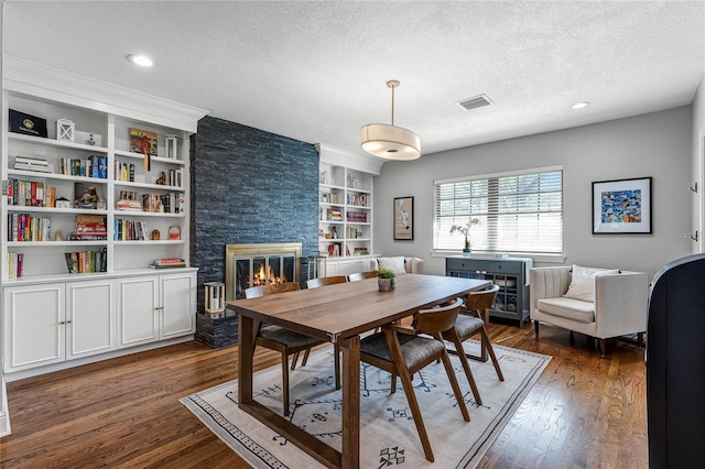 dining room featuring visible vents, built in features, a textured ceiling, dark wood-style floors, and a stone fireplace