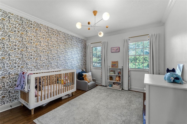 bedroom featuring wallpapered walls, crown molding, baseboards, wood finished floors, and a nursery area