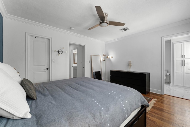 bedroom with a ceiling fan, visible vents, ensuite bath, dark wood-type flooring, and crown molding