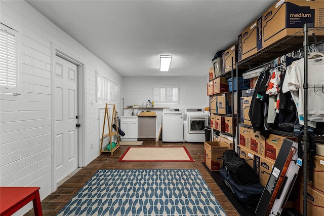 washroom featuring cabinet space, brick wall, dark wood-style flooring, and washer and clothes dryer