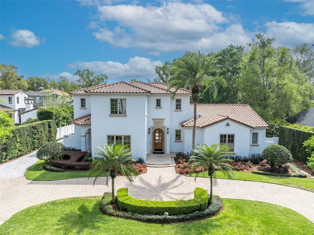 mediterranean / spanish house featuring curved driveway, a tile roof, a front yard, and fence